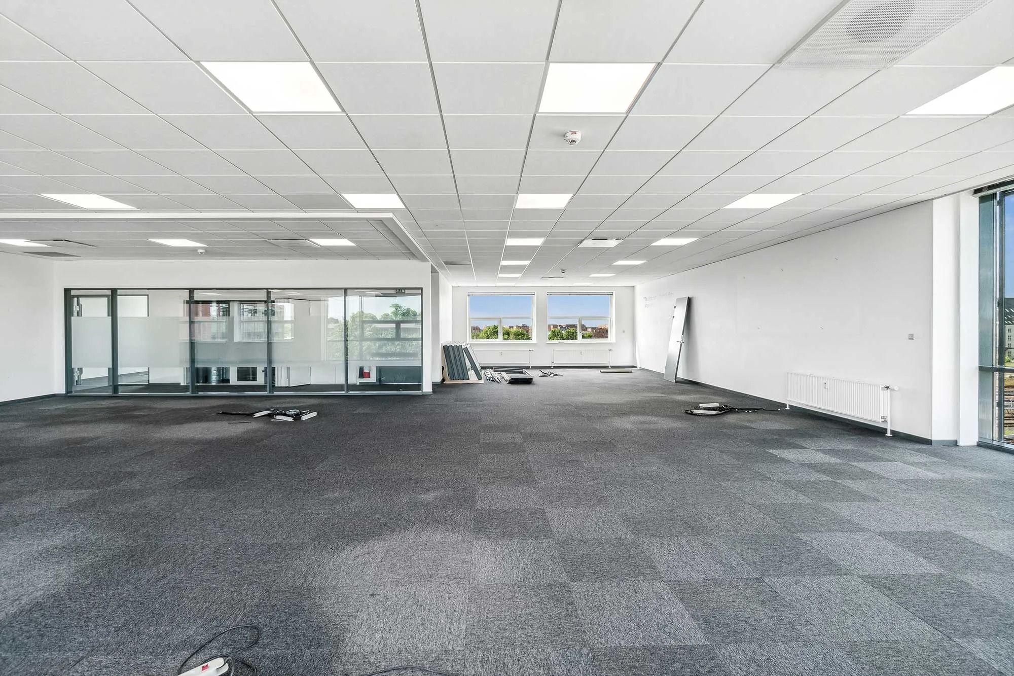 Kortere vægge med glasruder og hvide lofter i et tomt kontor. To stolpe er sat ned, og der er en søjle med hvidt papir på