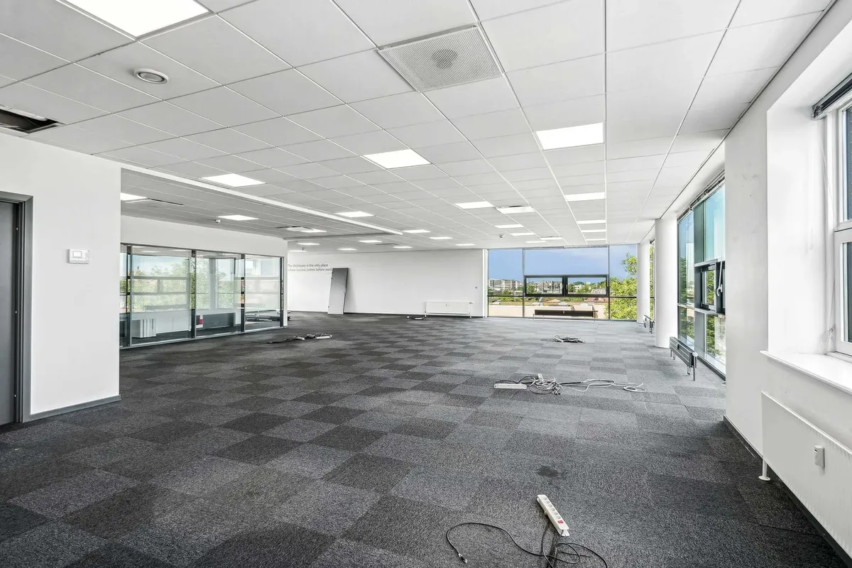 Et tomt kontorrum med en tæppegulv og glasvinduer med udsigt til byen og grønne træer