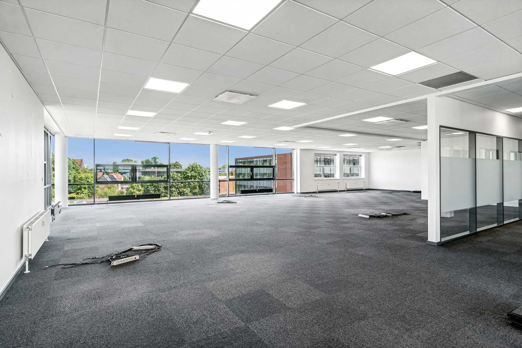 Forskudte elektriske kabler og radiatorer i et stort kontor med glasvinduer og loftsforhøjninger