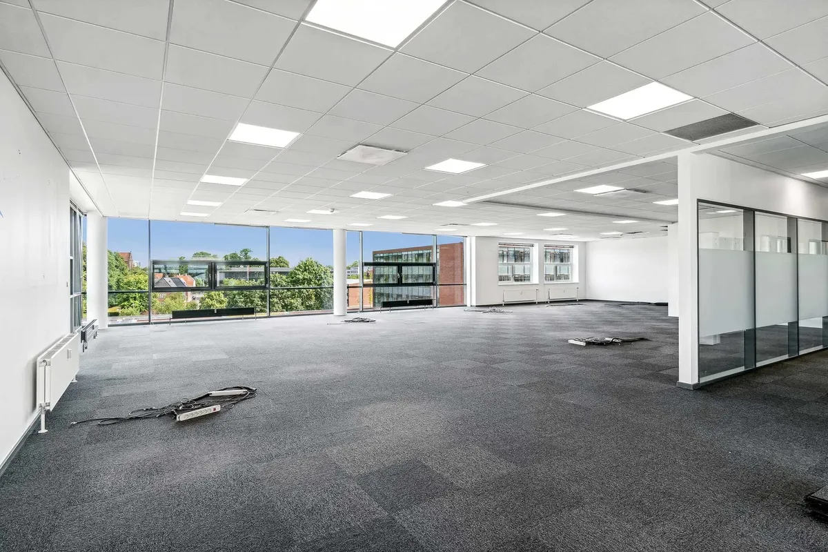 Forskudte elektriske kabler og radiatorer i et stort kontor med glasvinduer og loftsforhøjninger