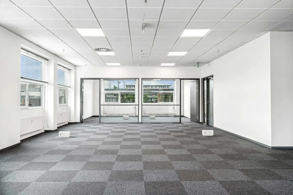 Store og lyse kontorlokaler med gulvbelægning, hvide vægge, glasdøre og vinduer med jalousier samt gulvstikkontakter