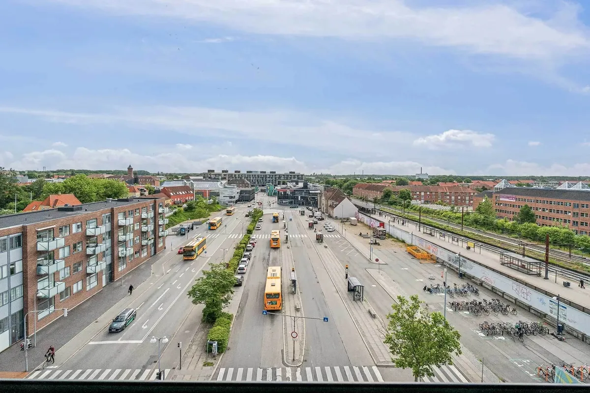 Busser og biler kører gennem en stor byvej med sporvognsspor og parkeringspladser på siderne