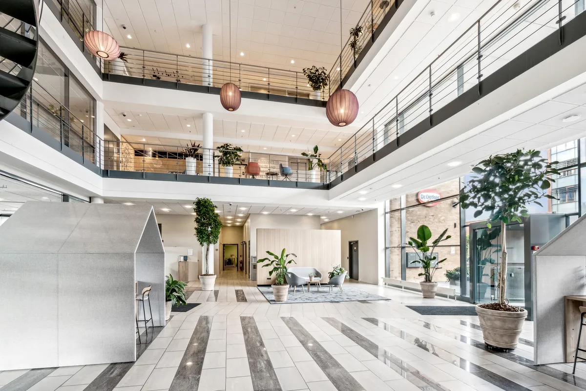 Kontor med terrasse og lyse loftsrum, lyse gulve og terrasse med bord, stole, sofaer, planter og møbler