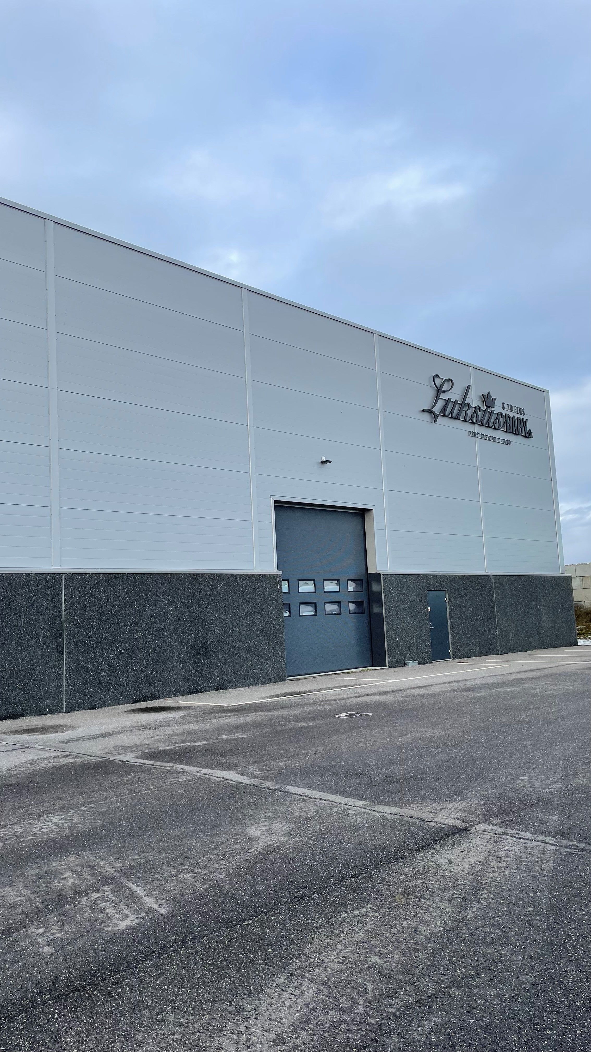 Luksusbabys bygning med skrifttypen Luksusbaby og Luksusbabys logo. En stor garagedør og en lille dør er på siden. En skygge