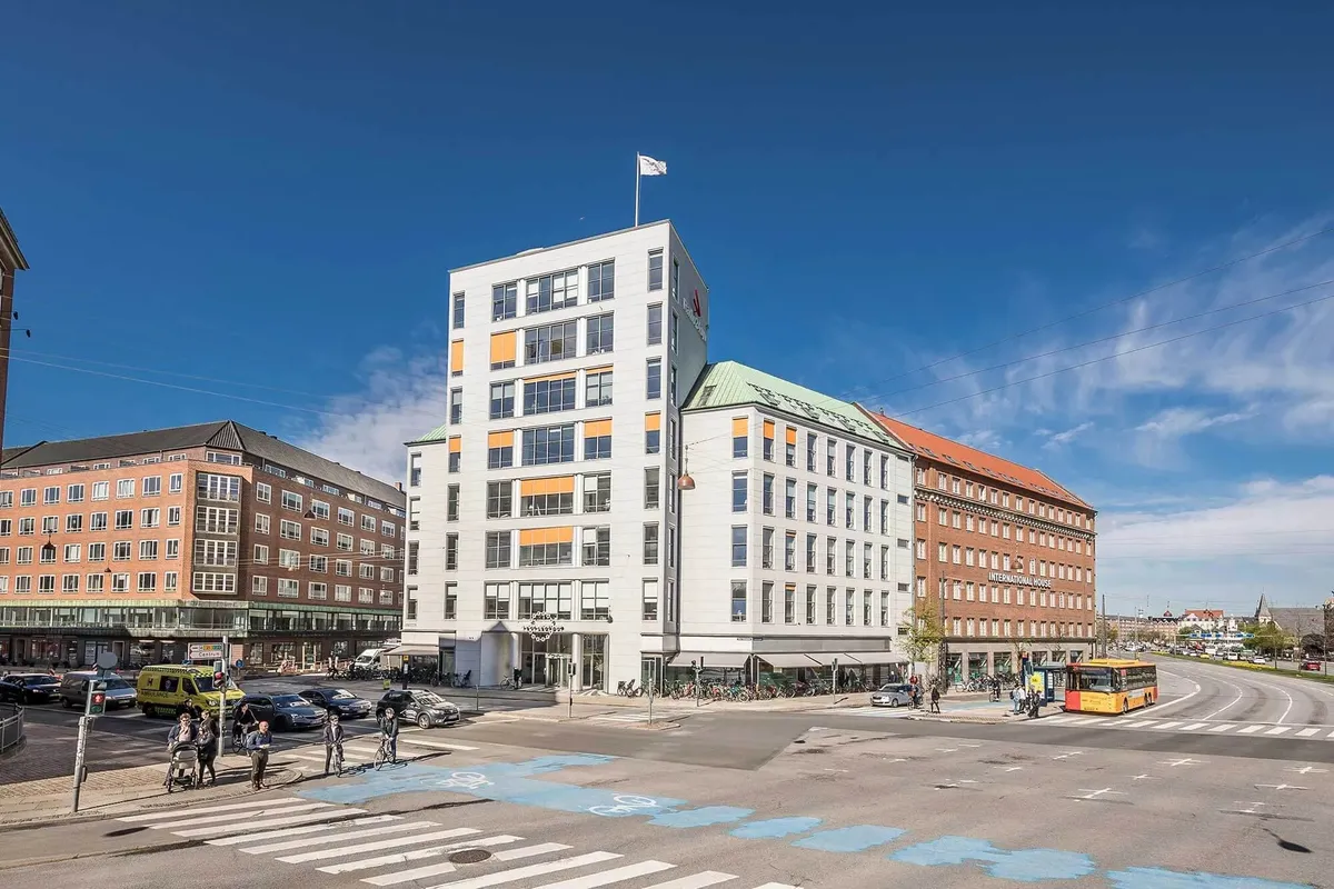 Forskellige bygninger og en stor gade med busser, biler og folk som går og cykler langs kanterne af gaden