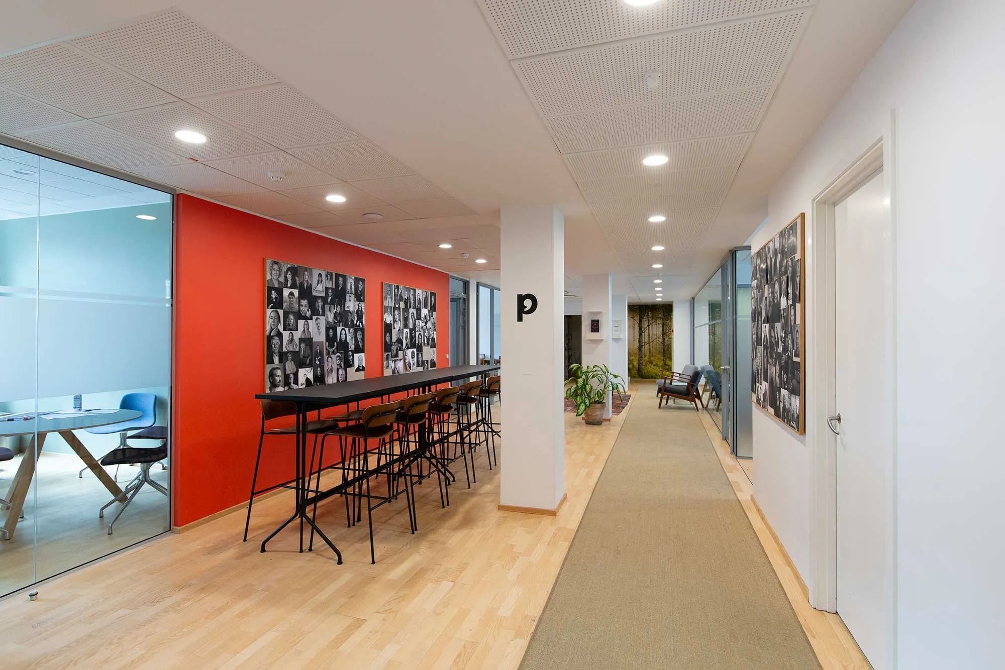 Kontorgang med fotokollage og mødebord på glas og træ, med gulvvæg og loftslamper