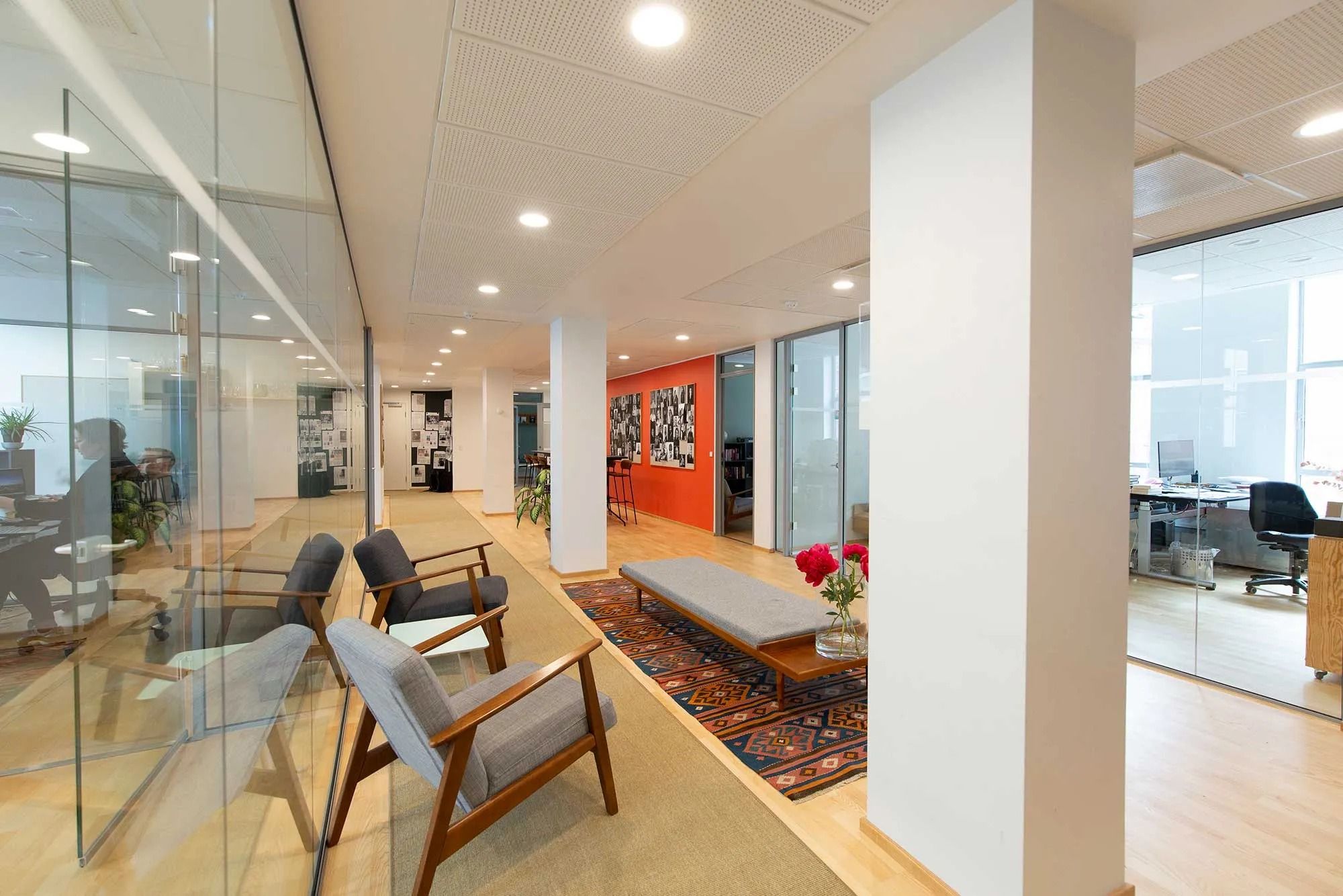 Moderne kontor med glasvægge, højloft og lyse loftslampe. Kontoret har røde vægge, hvid gulv og møbler og kunstværk i