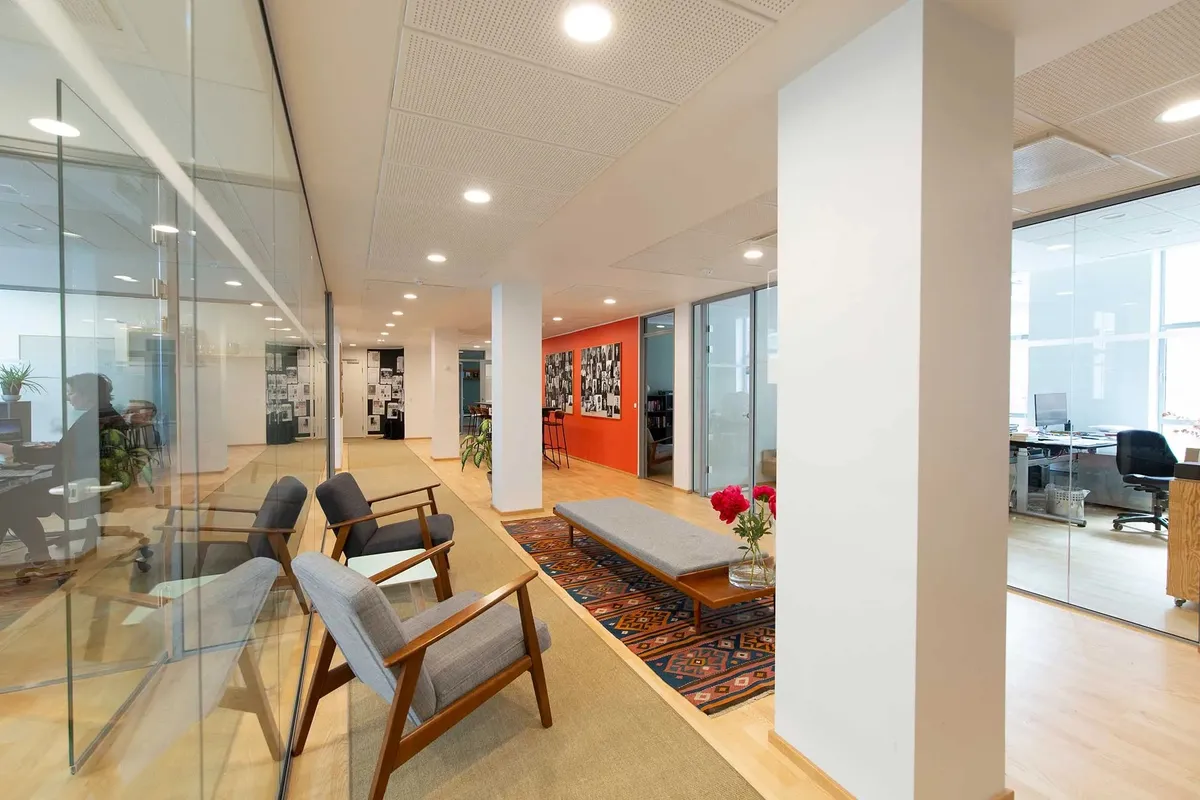 Moderne kontor med glasvægge, højloft og lyse loftslampe. Kontoret har røde vægge, hvid gulv og møbler og kunstværk i