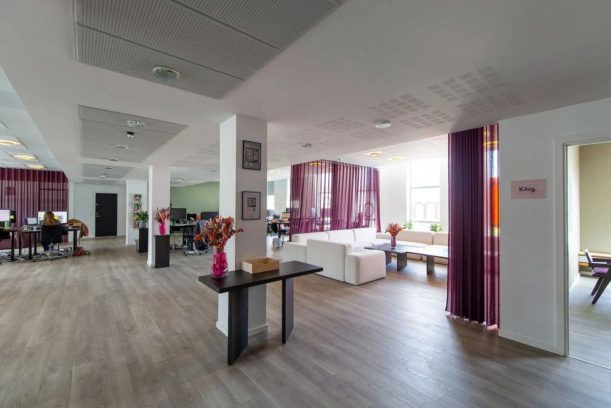 Kontorlokaler med moderne møbler og lyse vægge samt en sofa og et bord med blomster.