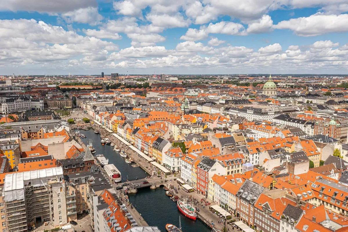 En luftoptagelse af København med gamle bygninger, røde tag og mange skibe i havnen, med folk der går på kajen og bygninger