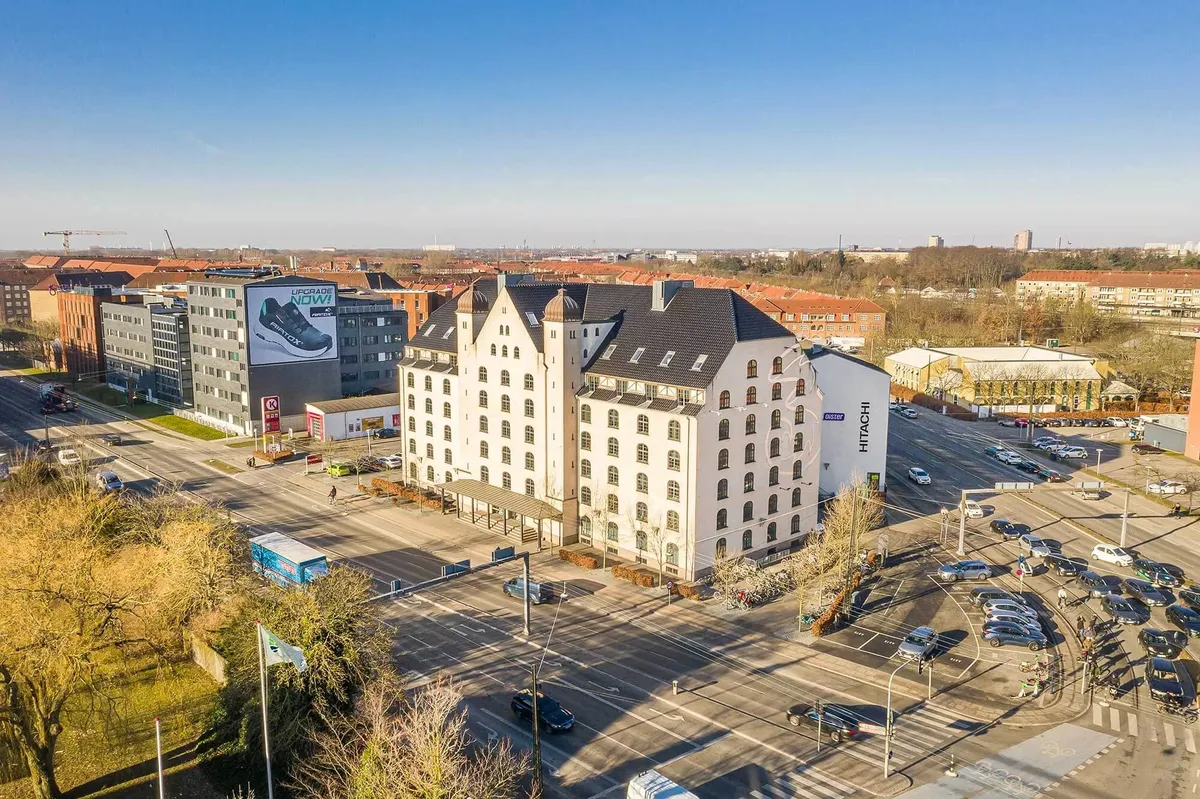 Højhus med kontorlejemål og parkeringsplads ved et kryds i et større byområde med trafik