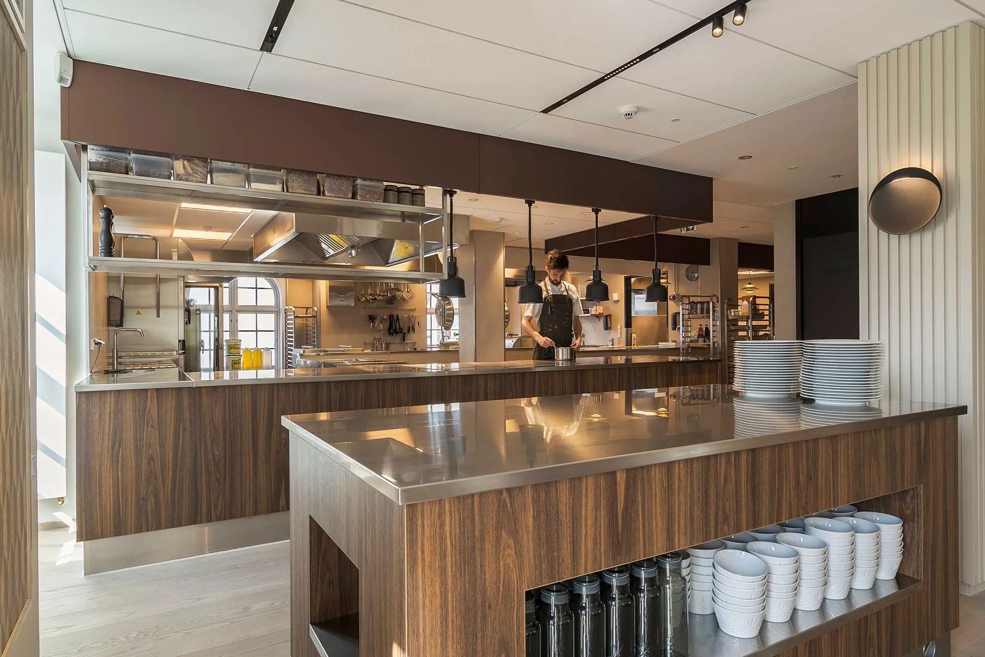 I moderne køkken med brædder og rustfrit stål er der en mand i sørøg med kogegrej og en stor skål på baren