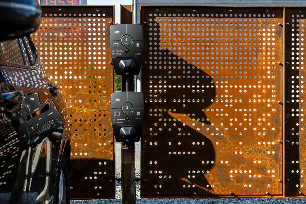 En elektrisk oplader til biler med nummer 1 og 2 samt teksten OK står fastgjort til en rusten metalpanel med huller