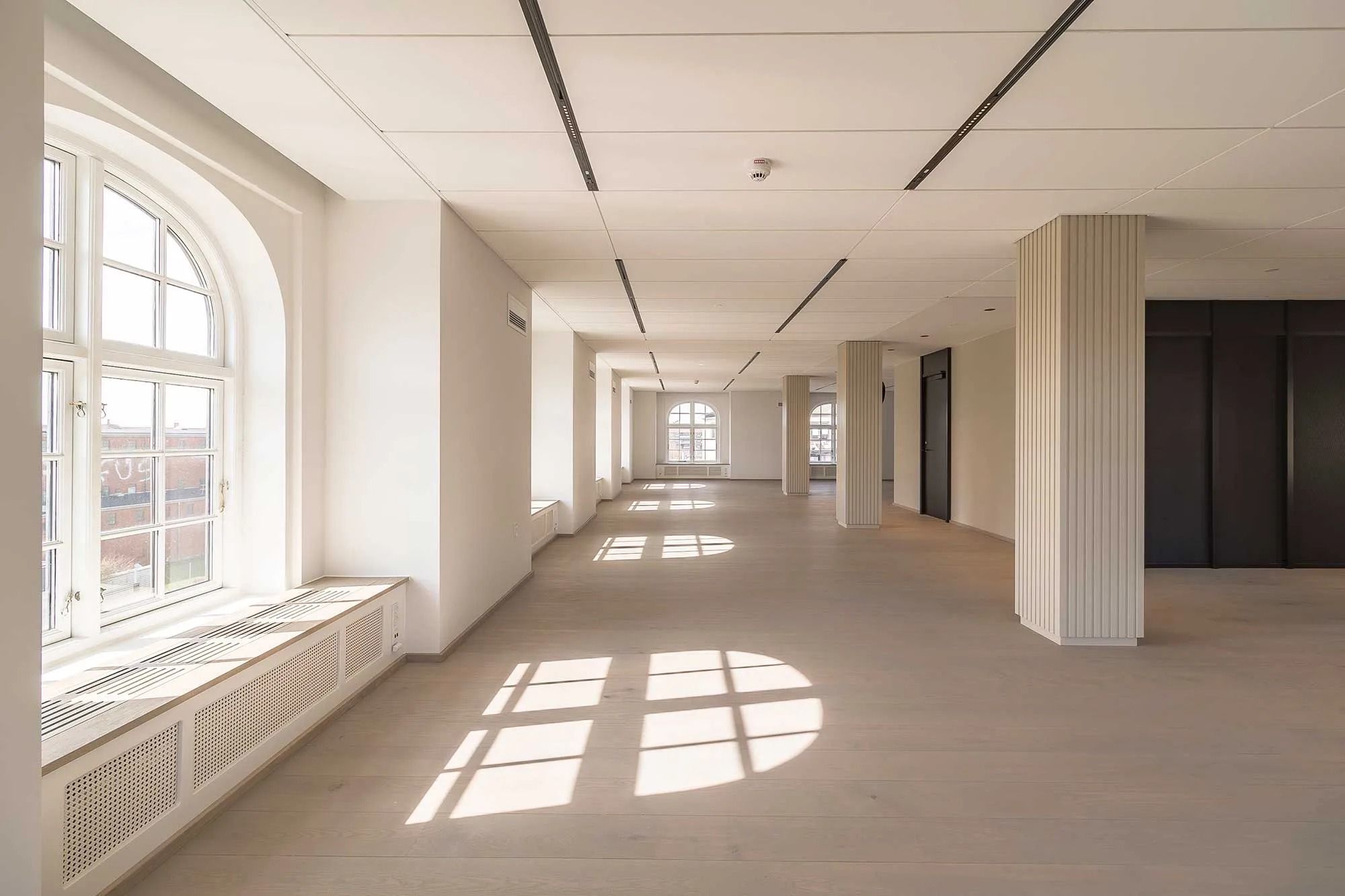 Moderne og ren interiør med lyse, hvide vægge og paneler, højt til loftet og store vinduer samt møbler og radiatorer