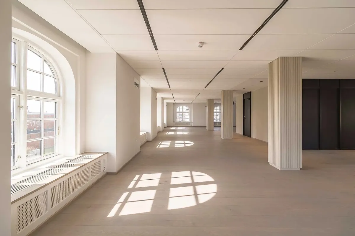 Moderne og ren interiør med lyse, hvide vægge og paneler, højt til loftet og store vinduer samt møbler og radiatorer