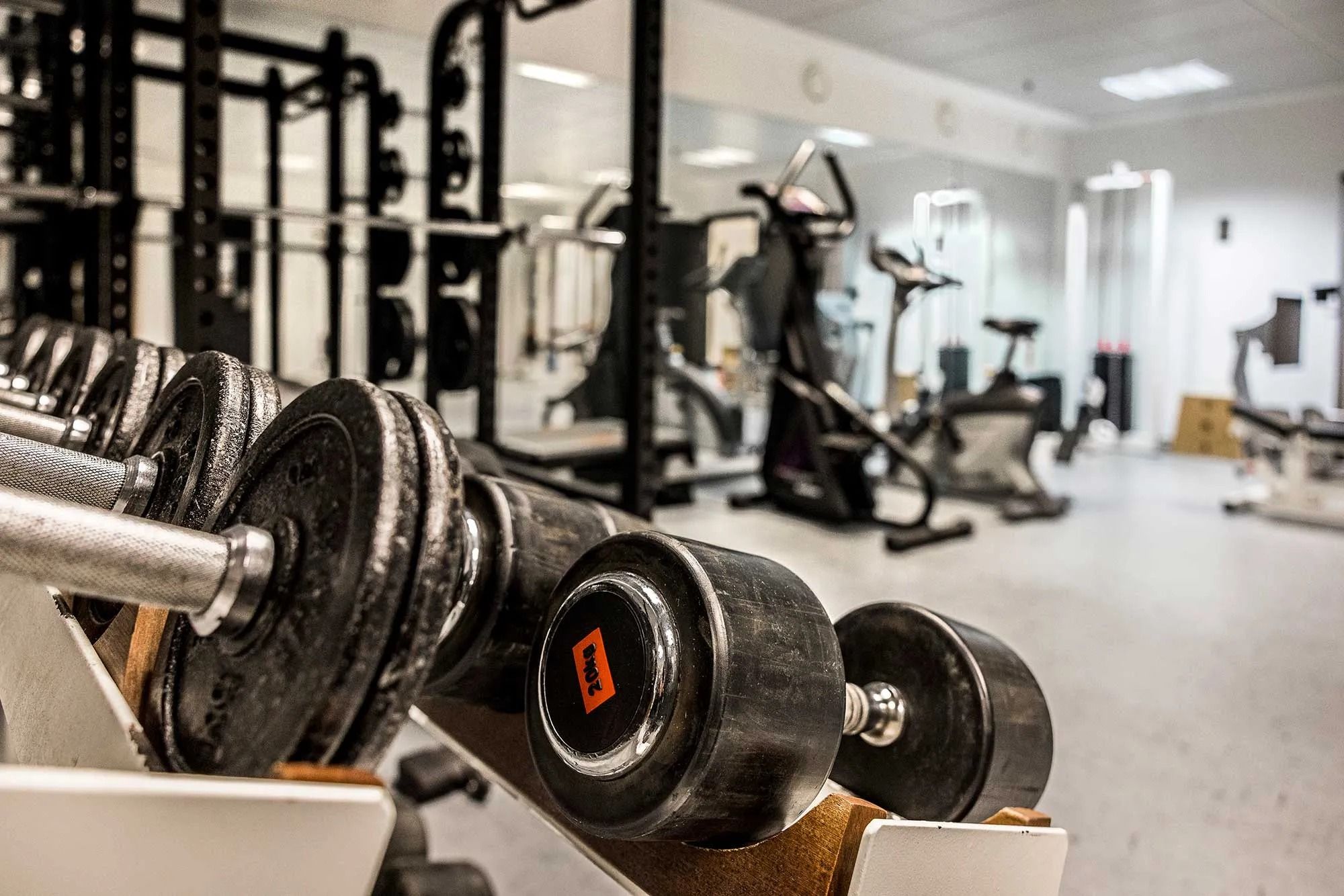 En række sorte vægtløfteshåndvægte med en rødt 20 kg-mærke og en række fitnessudstyr i en stor fitnesscenter