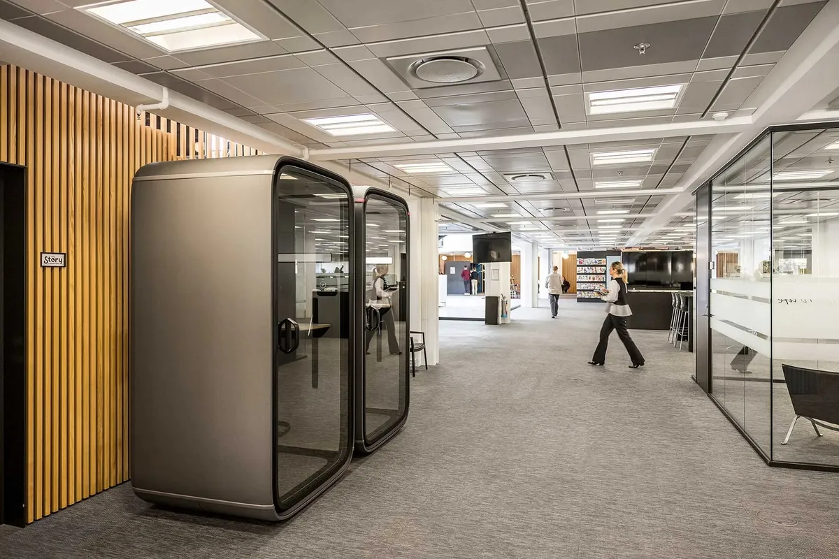 Et moderne kontor med to separate kabiner og flere folk i baggrunden som går og står