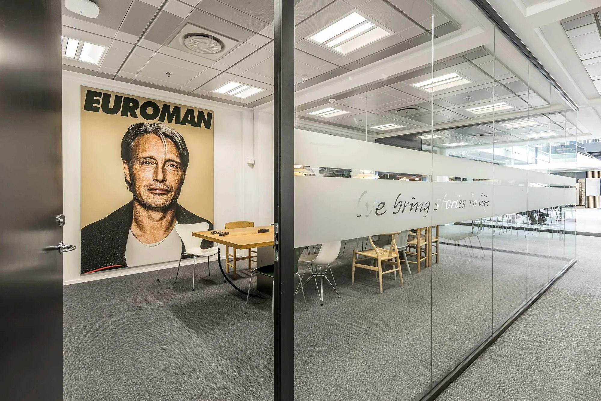 Kontorrum med møbelsæt og plakat med en mand i en jakke med teksten "Euroman"