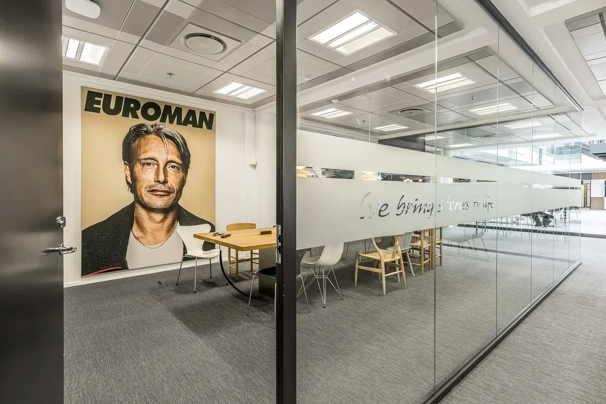 Kontorrum med møbelsæt og plakat med en mand i en jakke med teksten "Euroman"