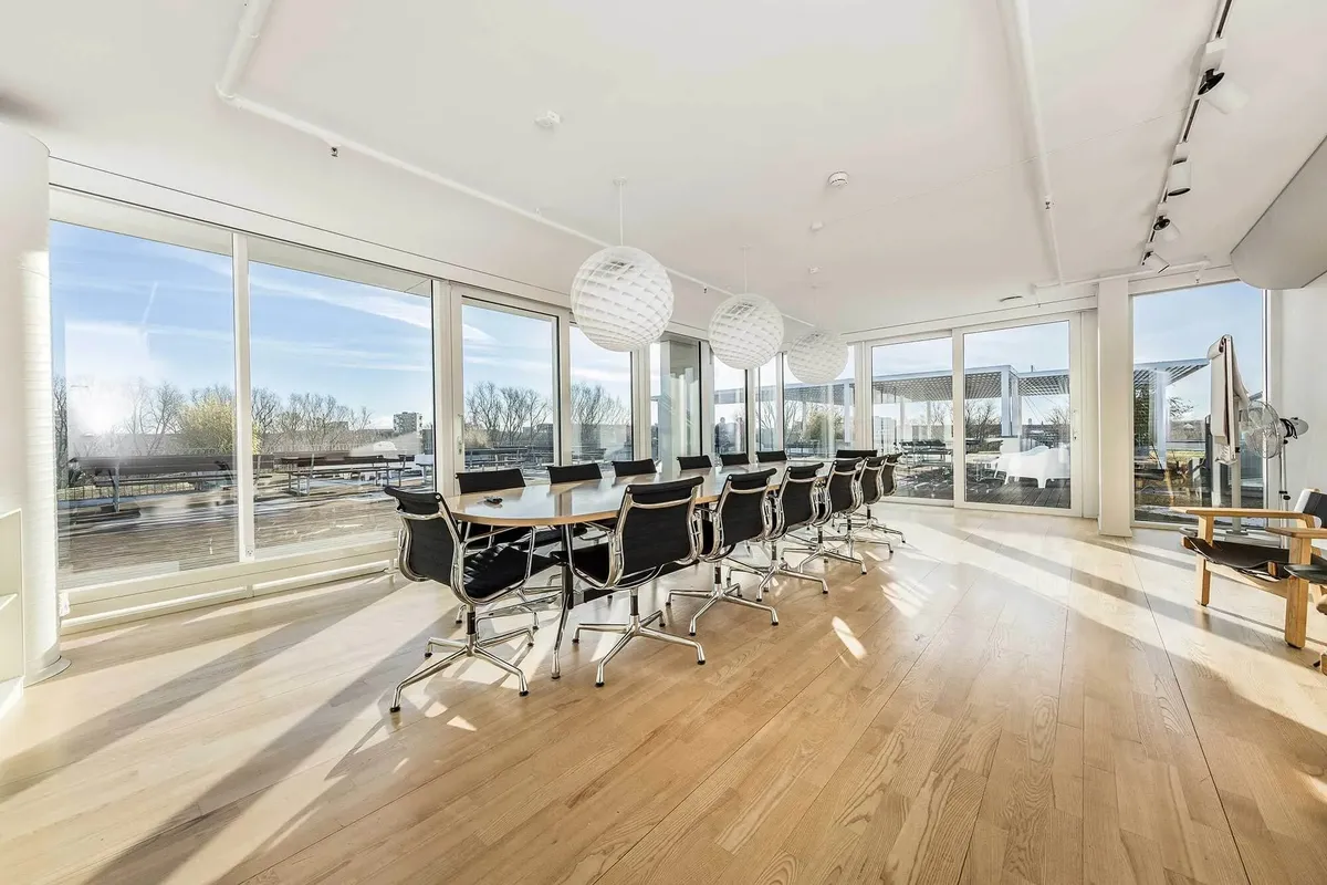 Kontor med stort bord og stole, store ruder, højloft og loftslampe samt stol med ståbord