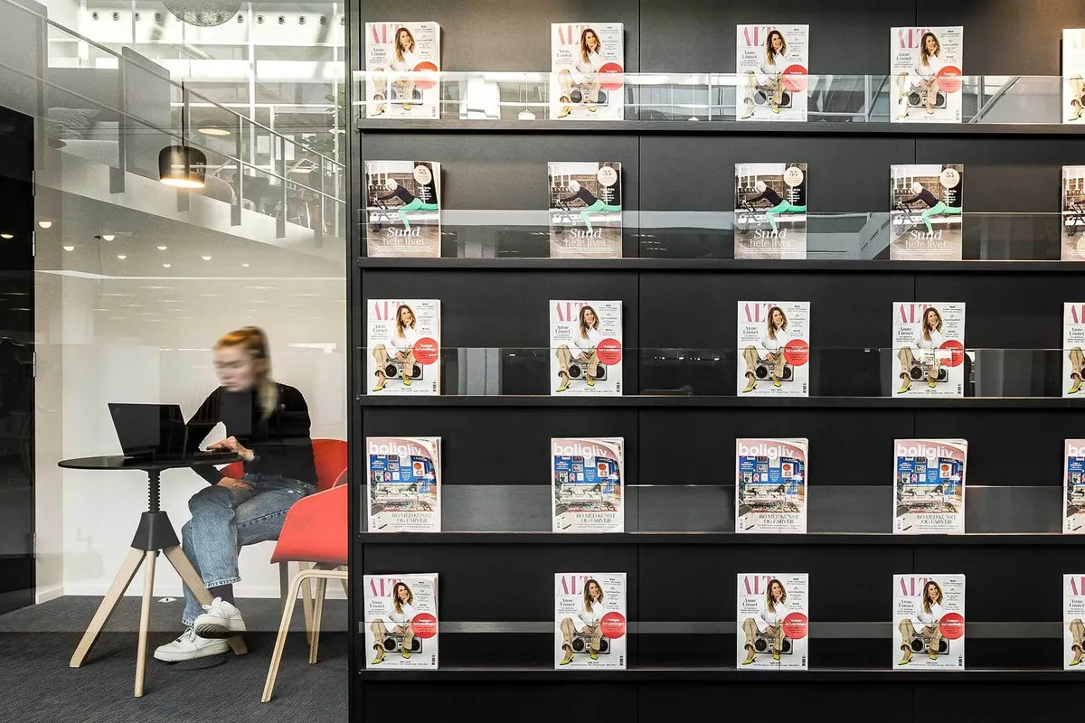 En kvinde sidder på en stol og bruger en bærbar computer i et kontor med store vinduer og lyse loftslampe