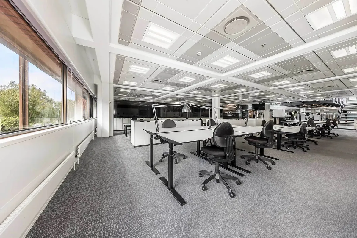 Kontorområde med moderne møbler og lyse vinduer, der giver masser af naturligt lys til arbejdsborde og loftslys