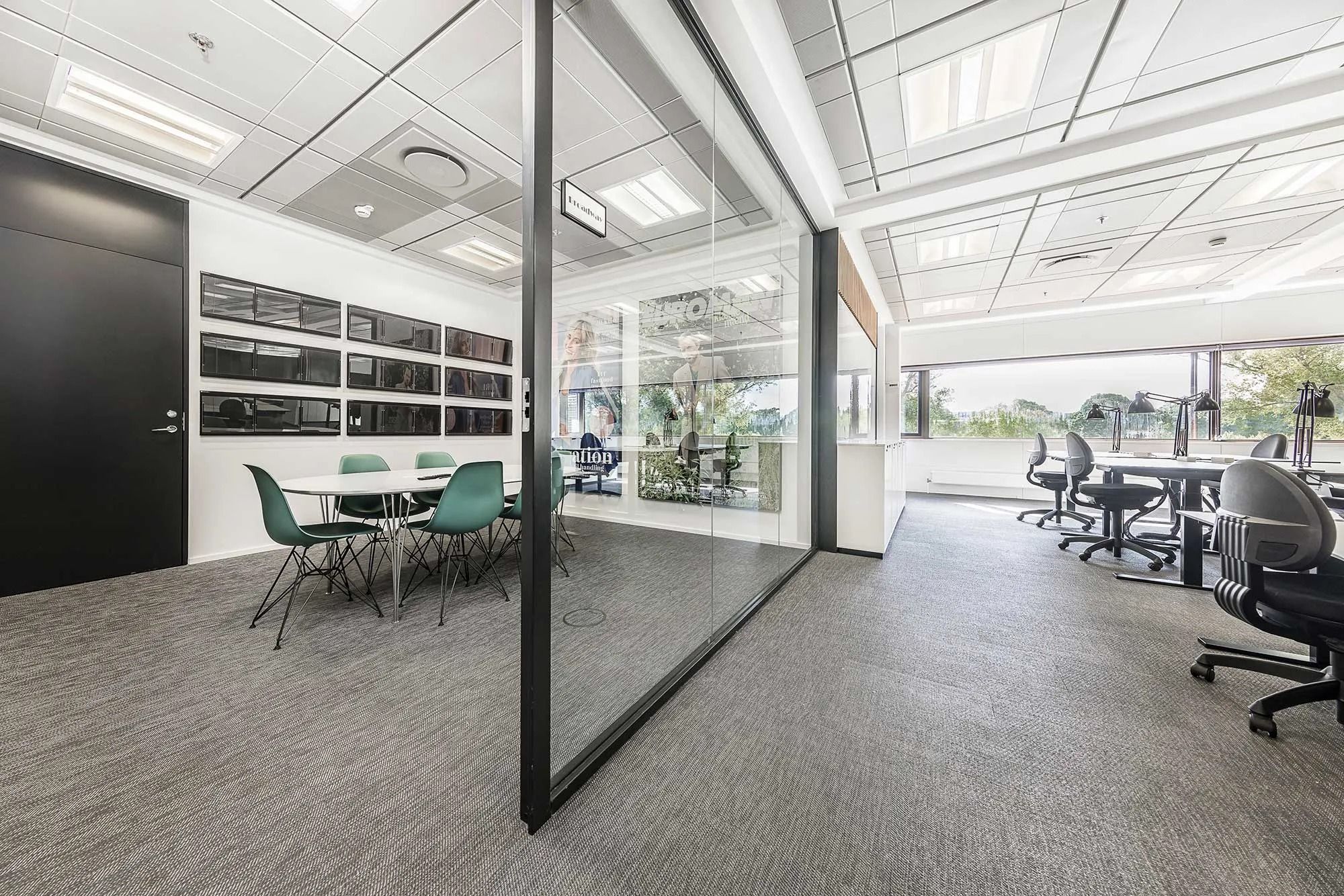 Moderne kontor med flere bordopsætninger og skriveborde med lysestole og en stor glasvæg