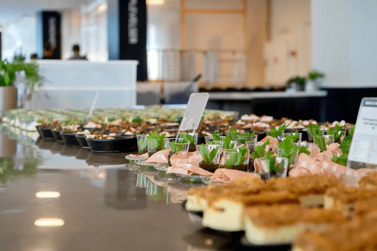 Buffet med fingermad og forretter på glas og små tallerkener i et moderne kontor med masser af grønne planter og moderne