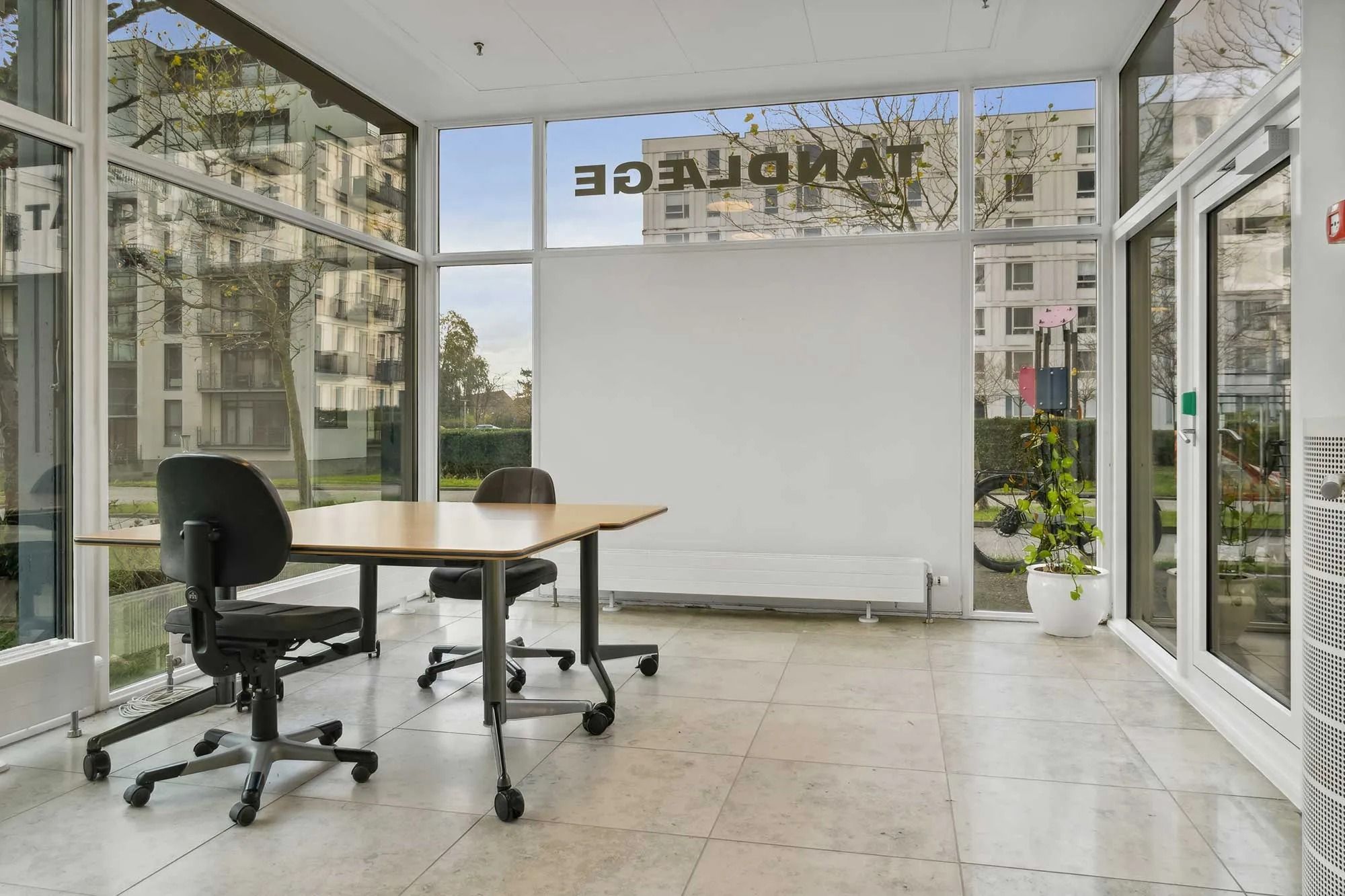 Kontor i moderne bygning med store ruder og slanke møbler i det indre rum. Bord og stole er placeret, og der er en stor