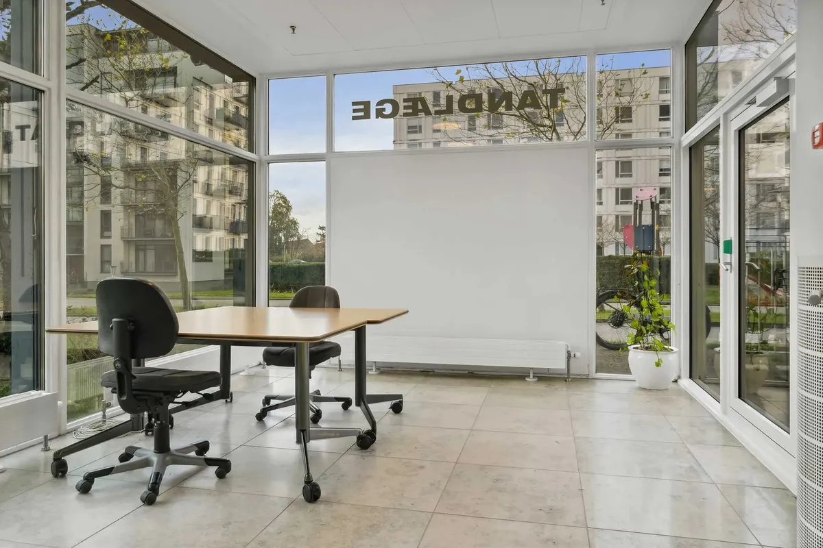 Kontor i moderne bygning med store ruder og slanke møbler i det indre rum. Bord og stole er placeret, og der er en stor