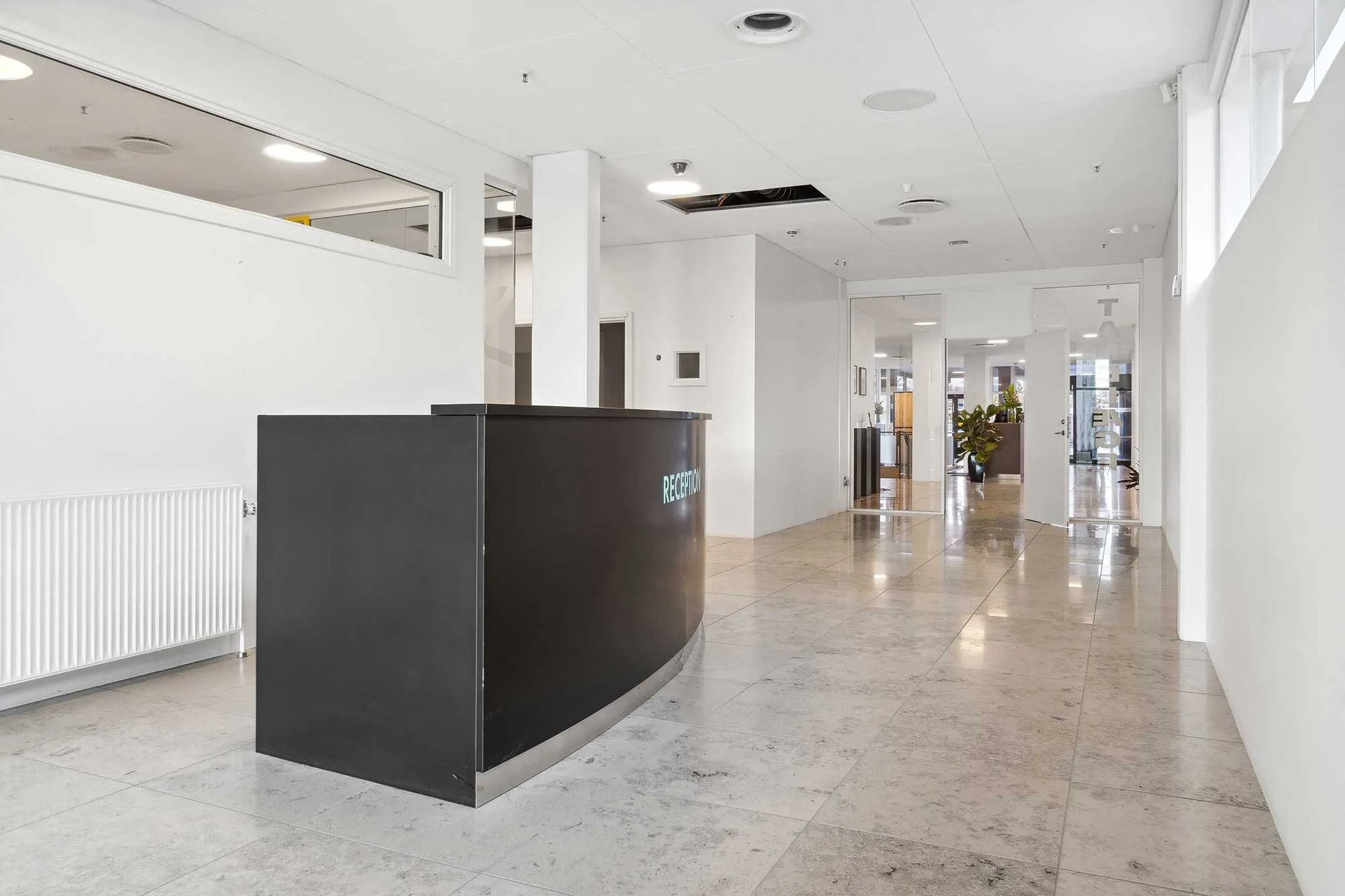 Indgangsområde i moderne kontor med marmorgulv og højloftede rum, der er udstyret med store vinduer og et elegant