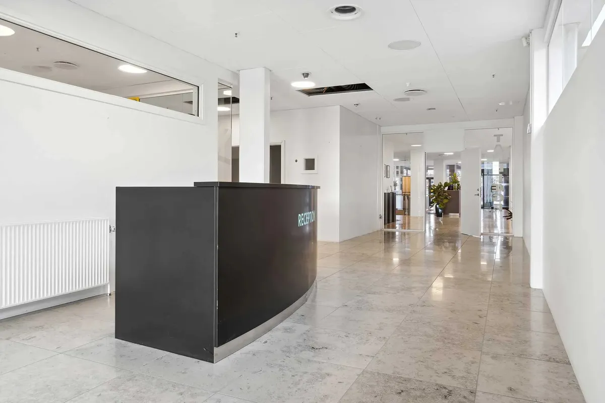 Indgangsområde i moderne kontor med marmorgulv og højloftede rum, der er udstyret med store vinduer og et elegant