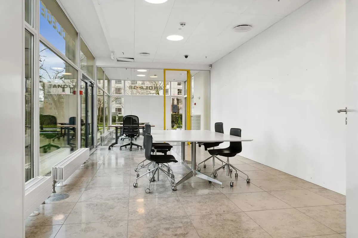 Moderne mødelokale med høj glasfacade og minimalistisk design. Runde hvide borde med høje stole og lysegule vægge