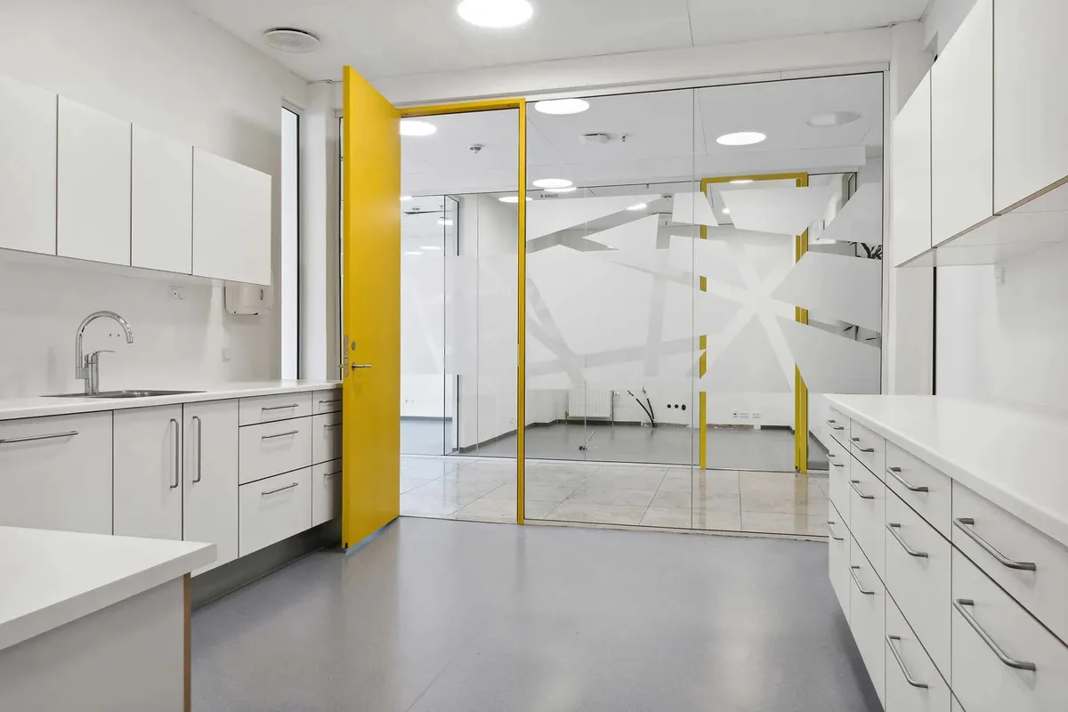 Moderne køkken med hvide skabe og lysegul dør og lysekroner på loftet samt en håndvask og et sæt skabe til