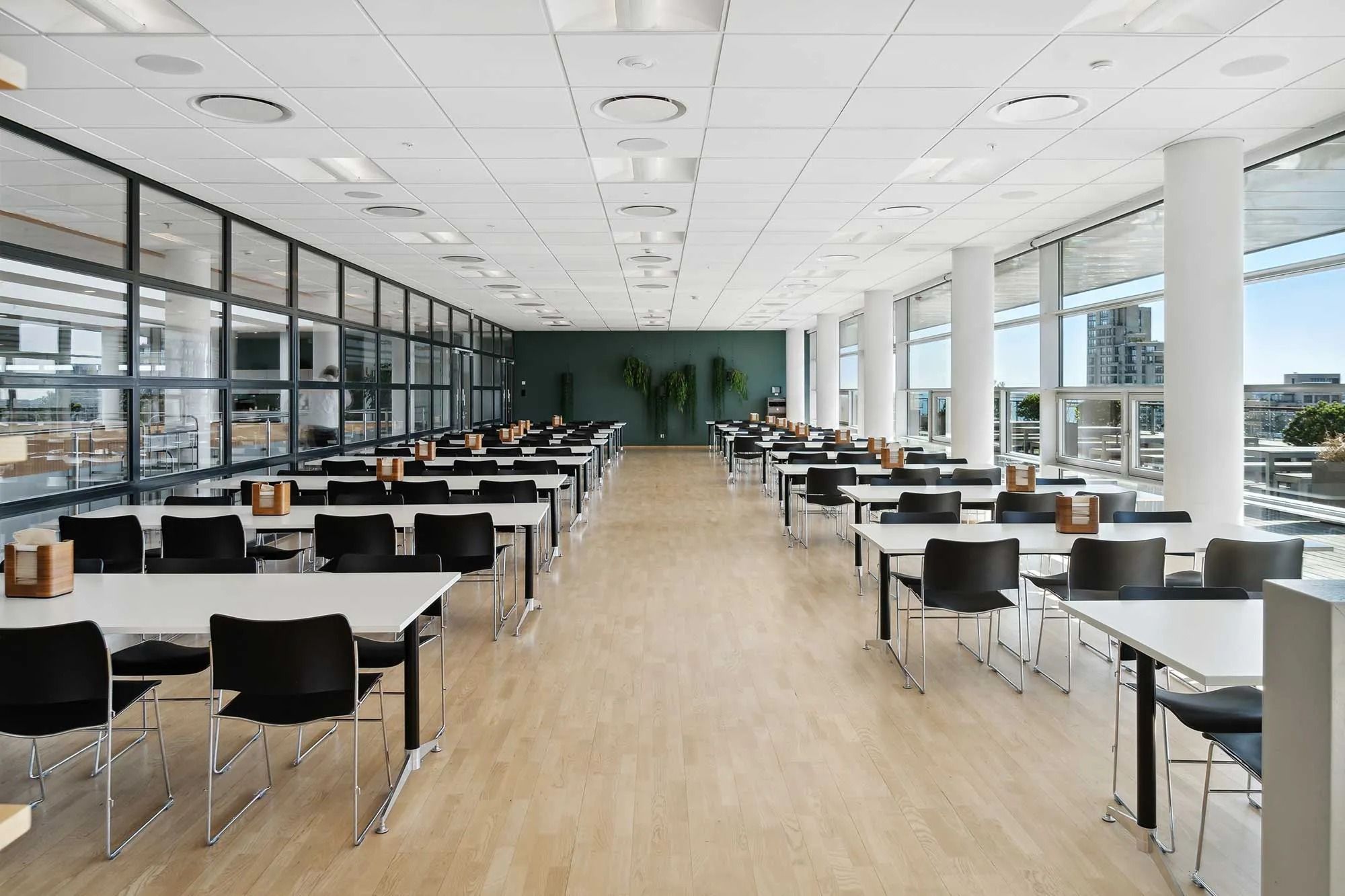 En stor åben fælles kantine med hvide borde og stole samt gulvet og store glasruder
