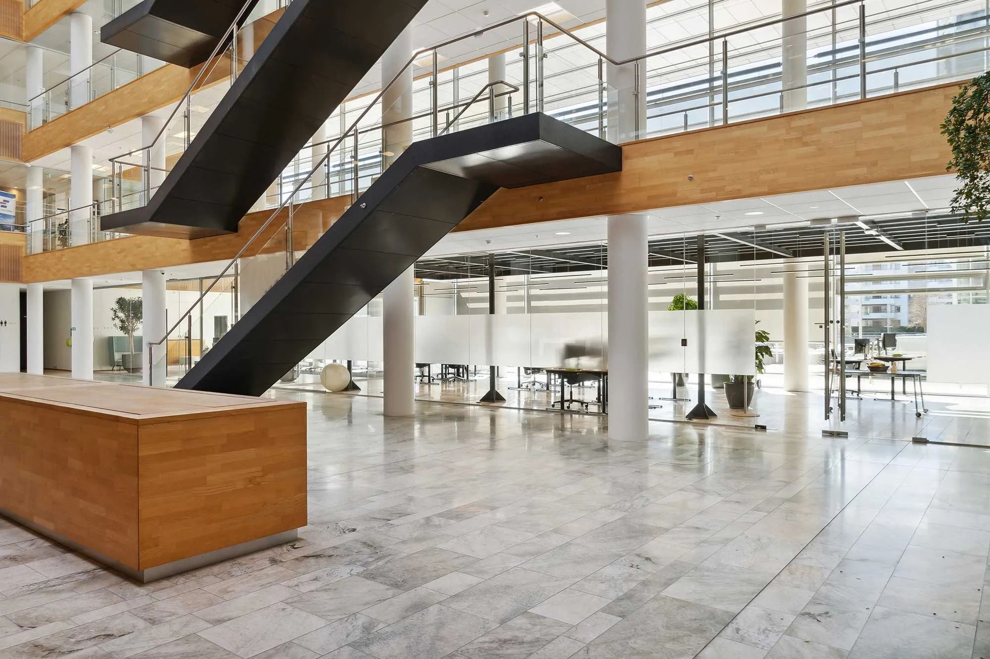 Åben lobby med marmorgulve, høje lofter, lysevinduer og slanke søjler og et stort skrånende trappeløb med glasgelændere