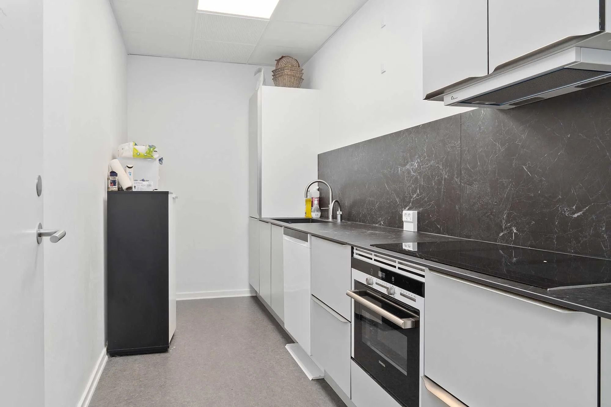 Minimalistisk køkken med hvide vægge og sort marmor og tælleplader. Sorte induktionskomfur, ovn og højt skur. Hvidt loft med