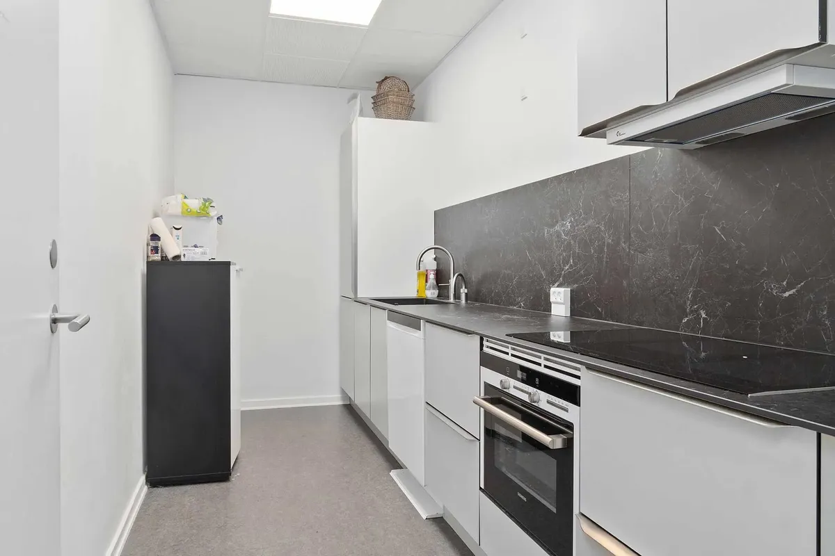 Minimalistisk køkken med hvide vægge og sort marmor og tælleplader. Sorte induktionskomfur, ovn og højt skur. Hvidt loft med