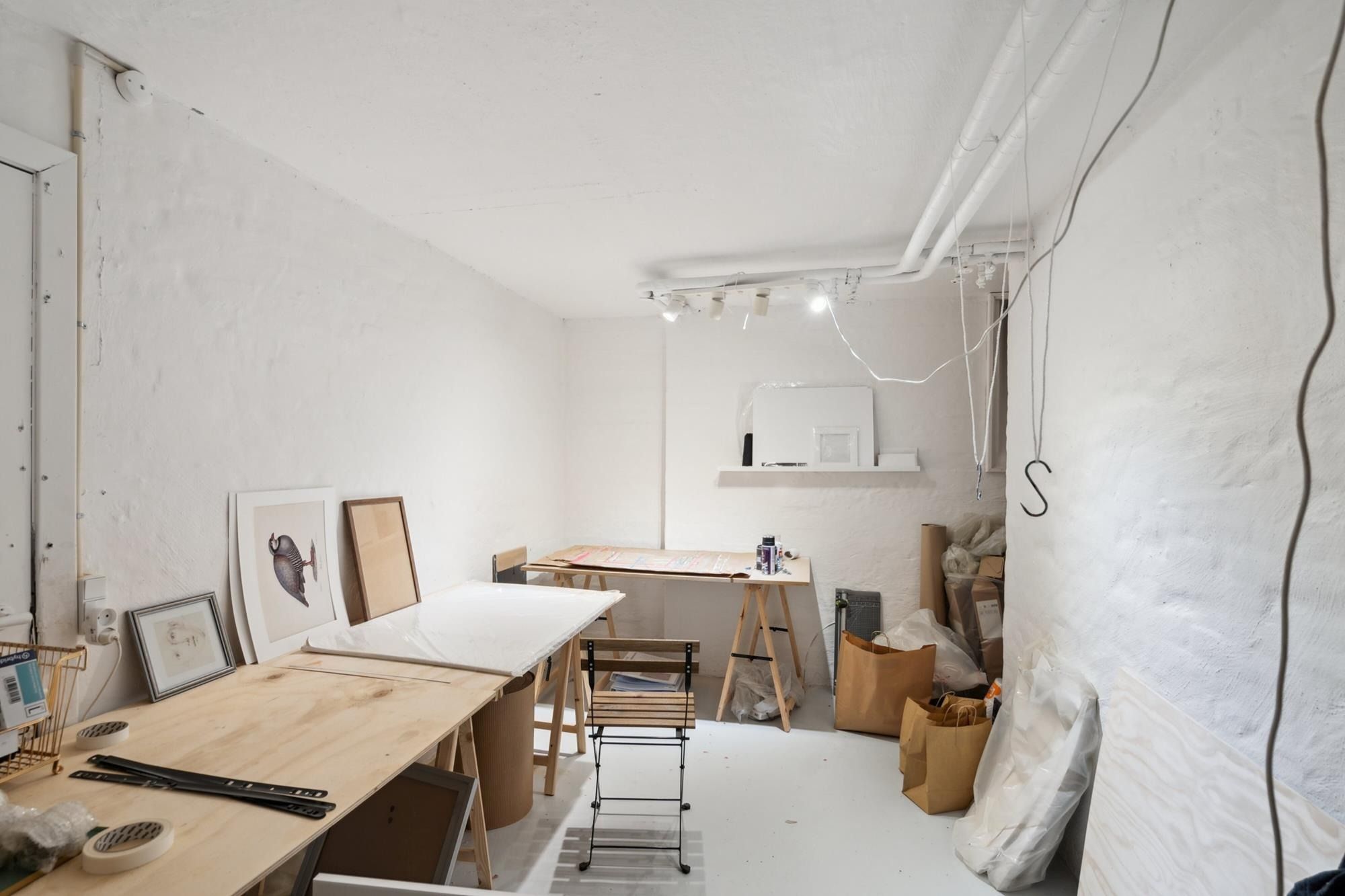 Et lille rum med lyse vægge og gulve, flere skriveborde og stole samt en række kunstværker og papirkurve