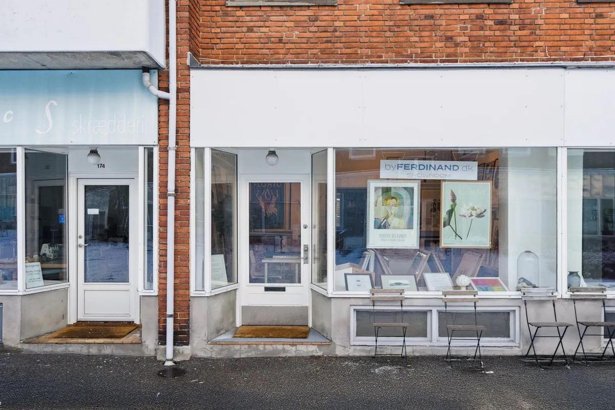 Kunstgalleriet by Ferdinand har lyse ruder og to små stole udenfor for at tiltrække kunder. Galleriet har kunstværker og en