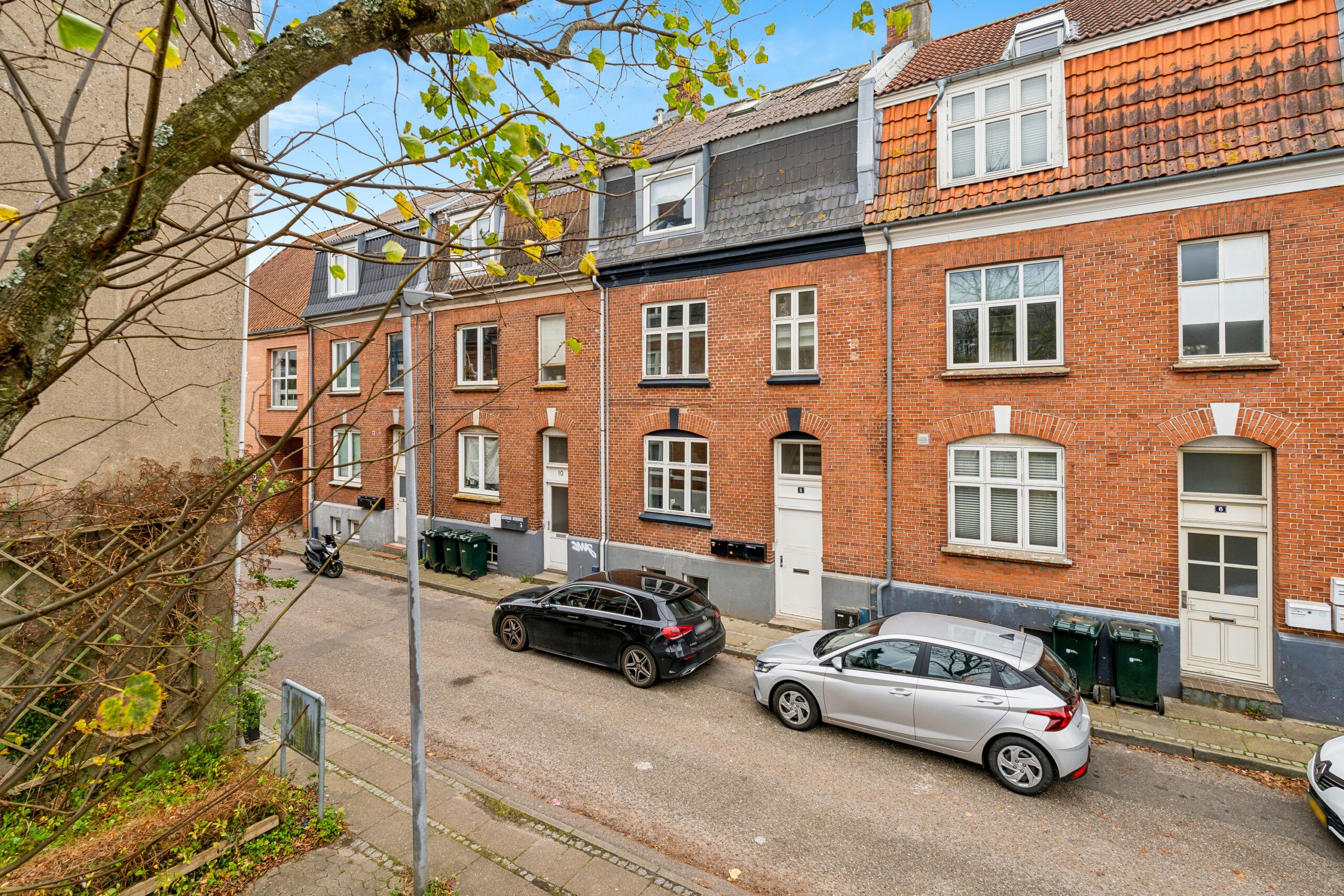 3 biler parkeret foran en række huse i Kolding, alle huse har hvide døre og røde tag
