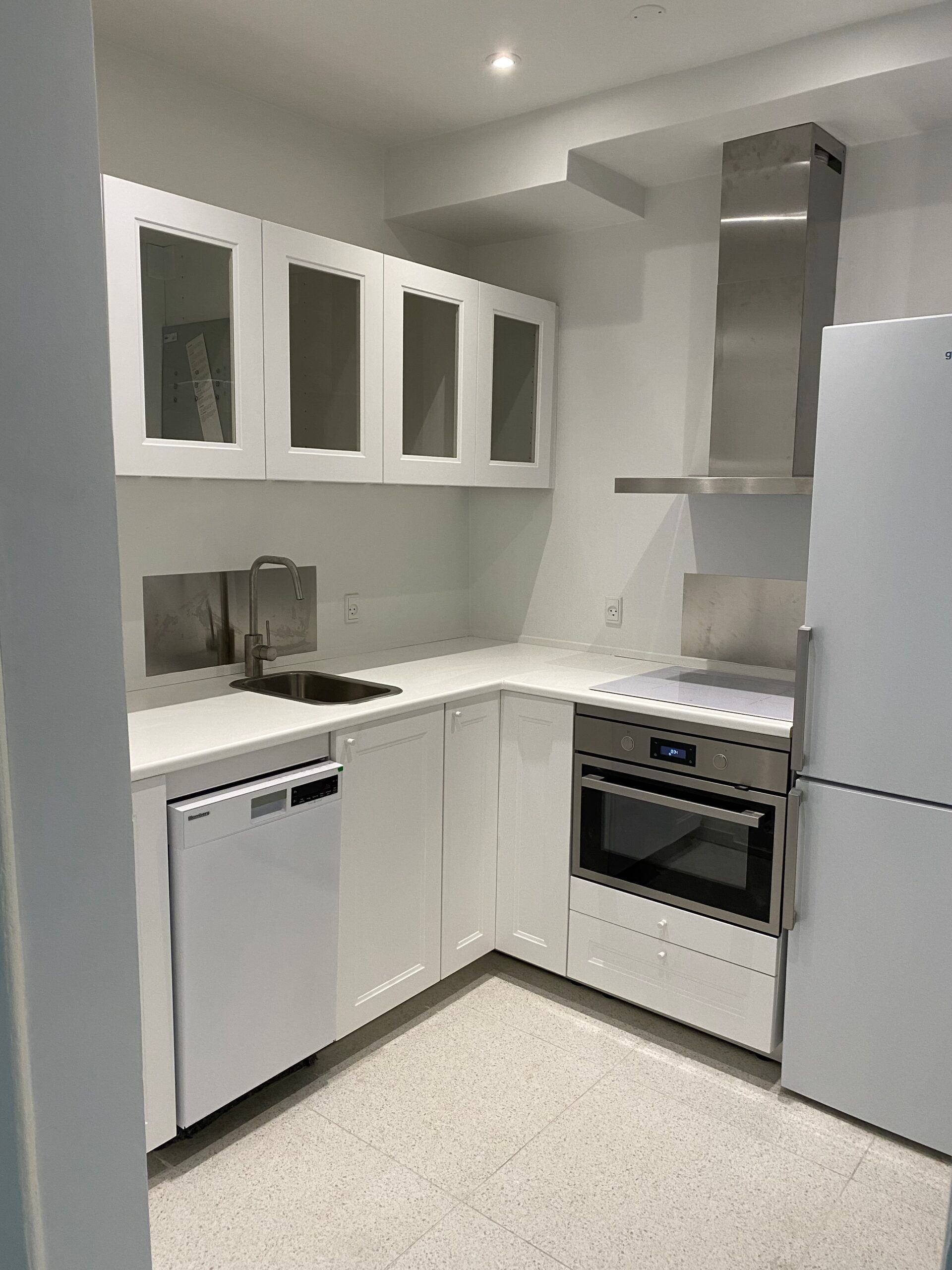 Rent og moderne køkken med lyse hvide vægge, moderne hvide skabe, lyse gulvfliser, hvid køleskab, moderne gaskomfur, lysegrå