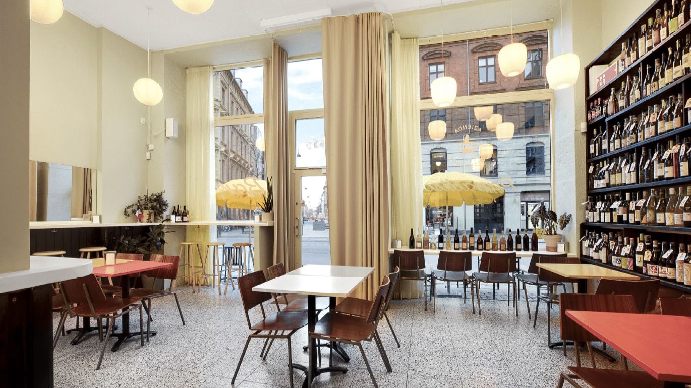 Nyrenoveret køkken med store vinduer og lysegule parasoller, flere borde og stole, et regneark, vinduer med byudsigt, et