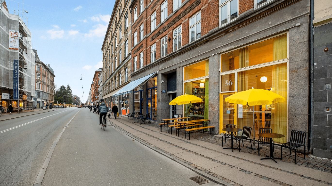 En cykelkørende mand passerer forbi en bygning med et gult paraply og bord og stole udenfor