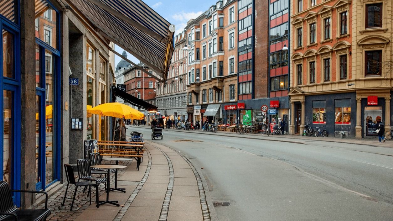 En tom gade med smukke bygninger og terrasser med gule parasoller og stole og borde