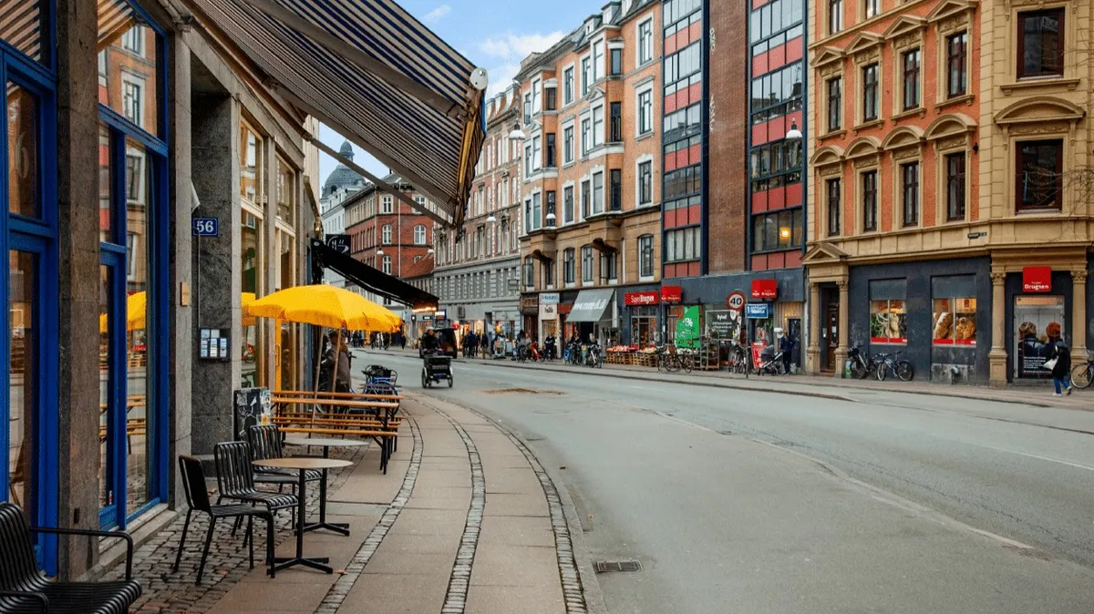 En tom gade med smukke bygninger og terrasser med gule parasoller og stole og borde