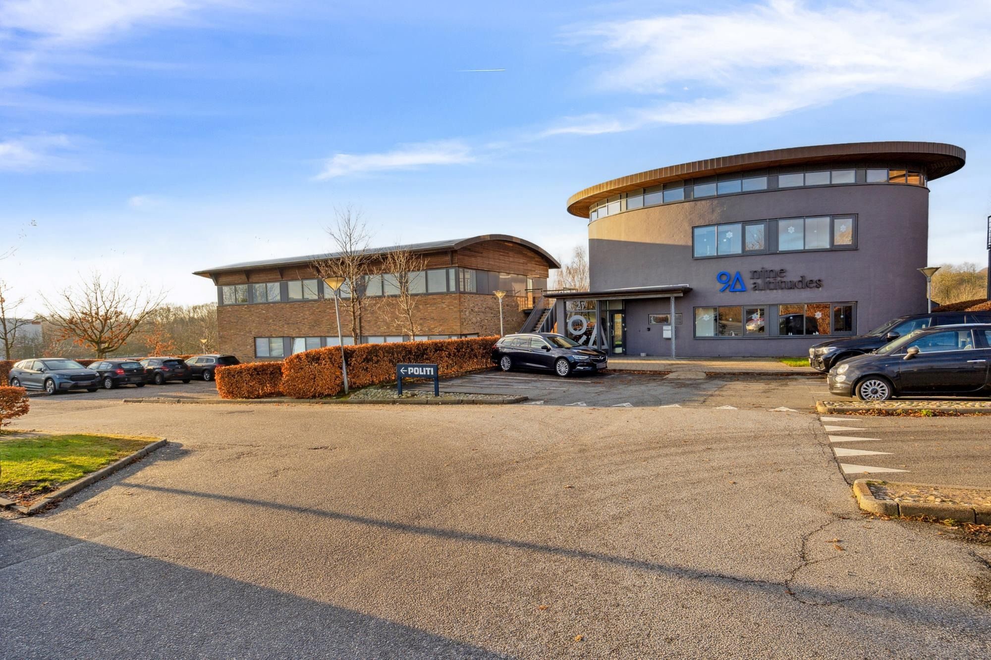 Moderne kontorejendom med solpaneler og skrånende tag i Aarhus, fire biler parkeret foran og adgangsskilt til venstre