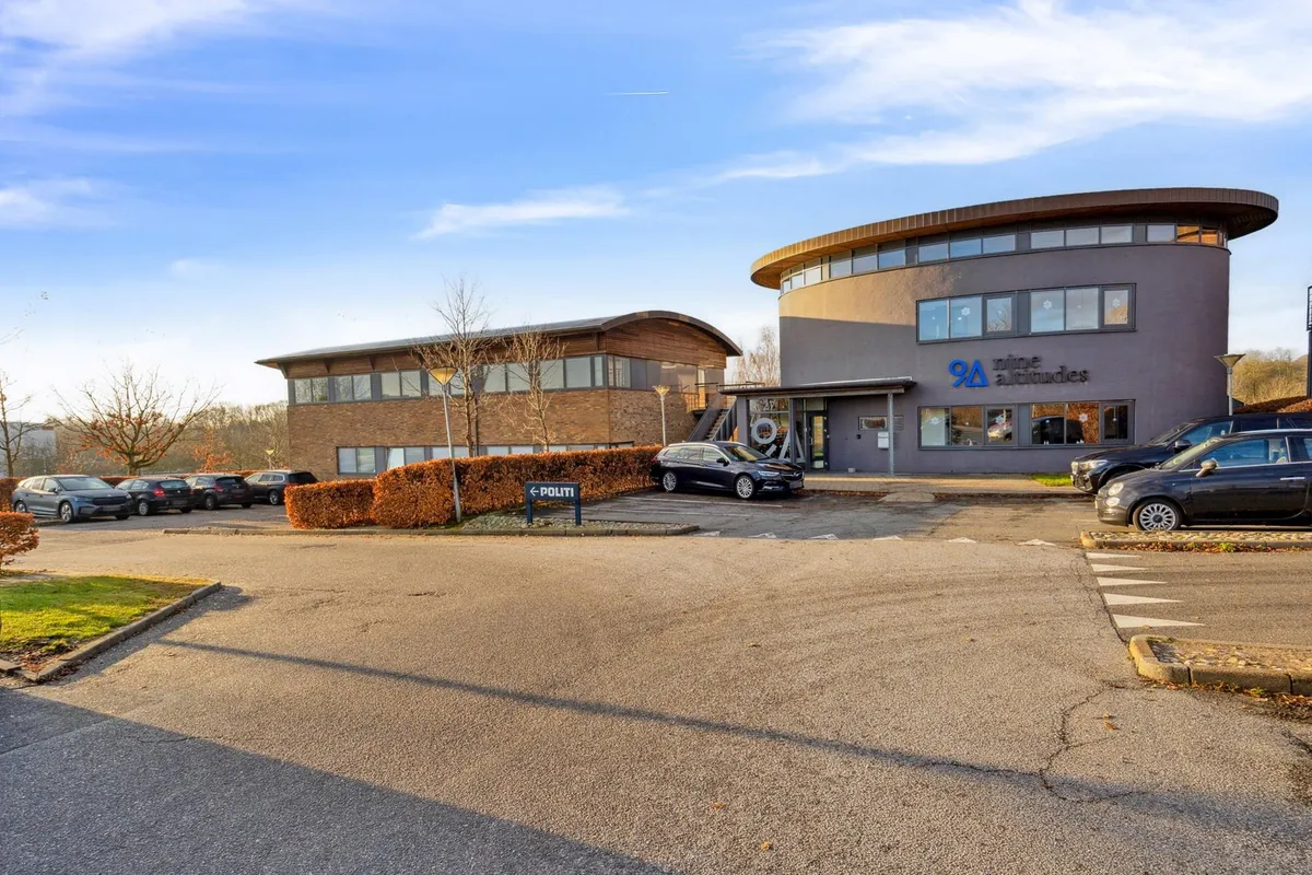 Moderne kontorejendom med solpaneler og skrånende tag i Aarhus, fire biler parkeret foran og adgangsskilt til venstre