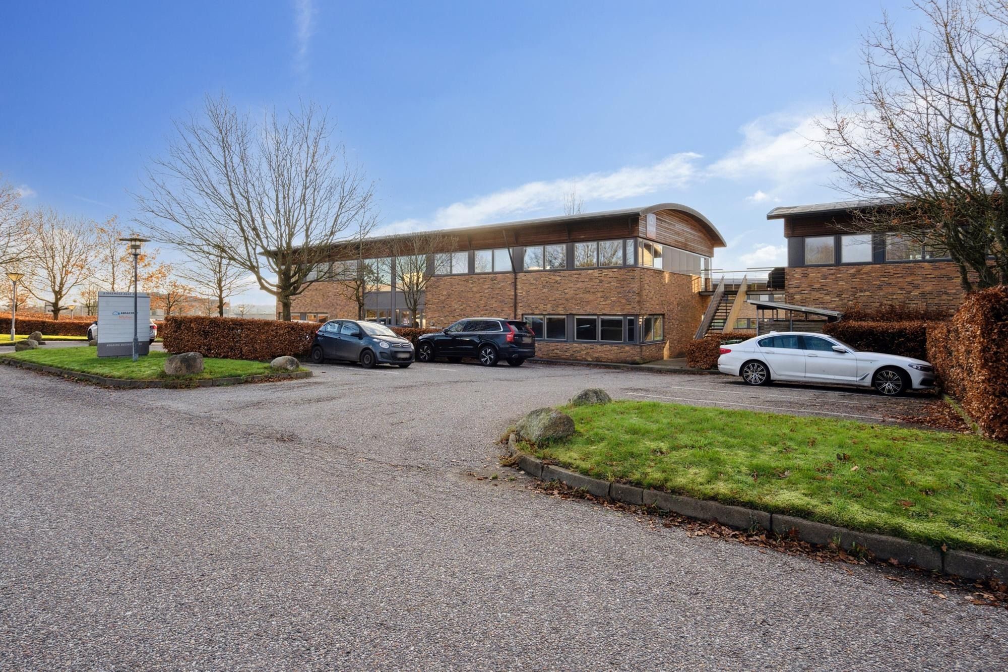 Moderne kontorejendom med parkeringsplads og tre parkerede biler og stærke lejerprofiler