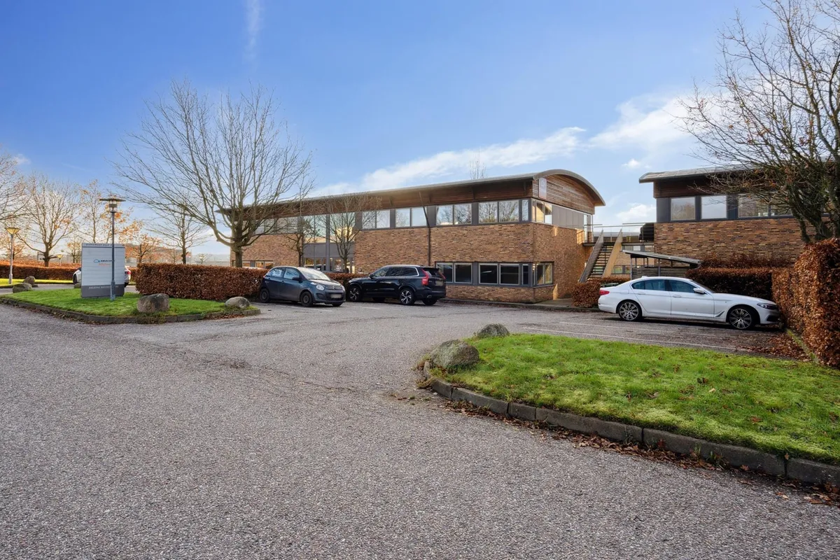 Moderne kontorejendom med parkeringsplads og tre parkerede biler og stærke lejerprofiler